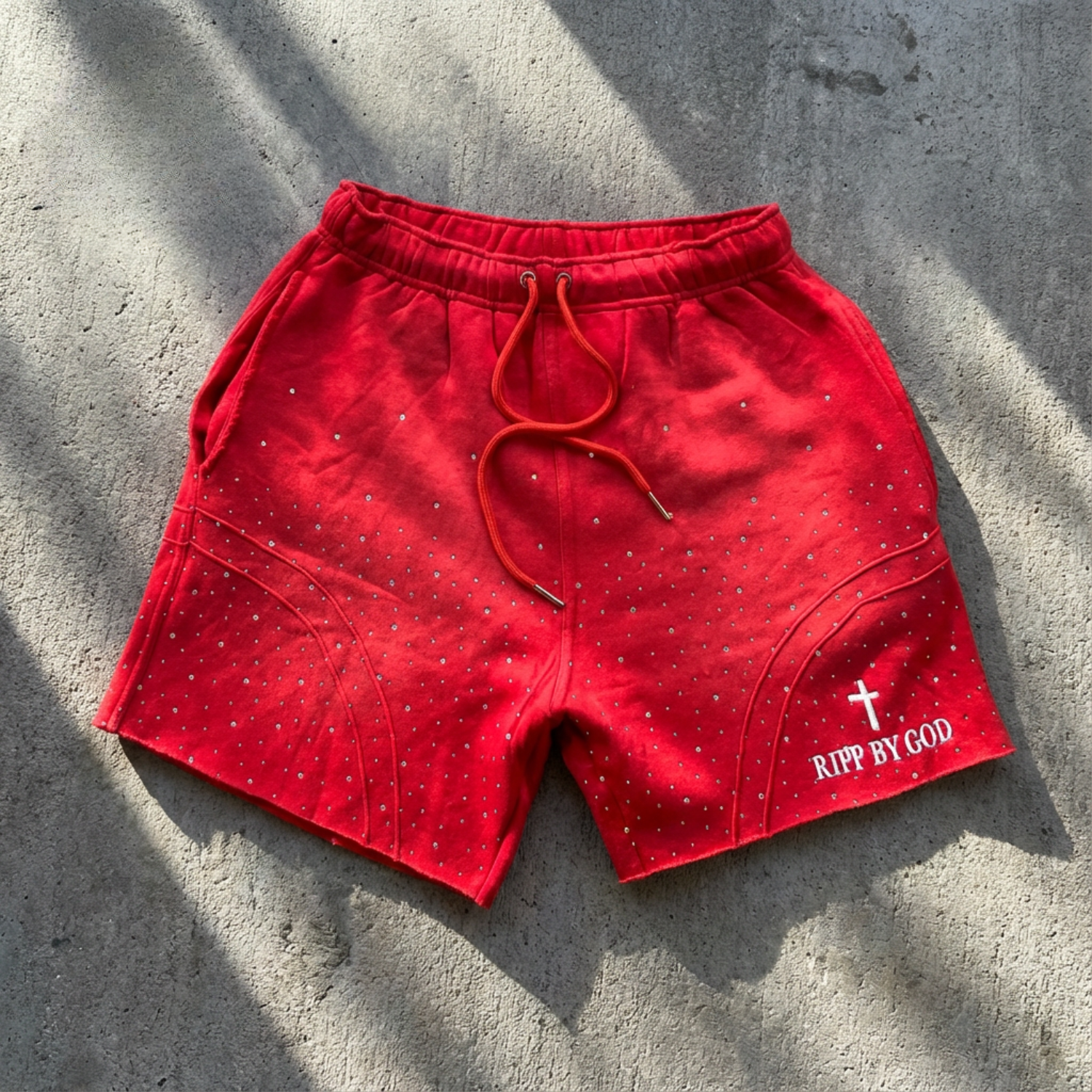 Red shorts with 'RIP BY GOD' text on a concrete surface