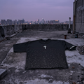 Black long-sleeve shirt with a white cross on a rooftop at dusk